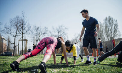 Calisthenics class at outdoor gym, instructor supporting women practicing yoga